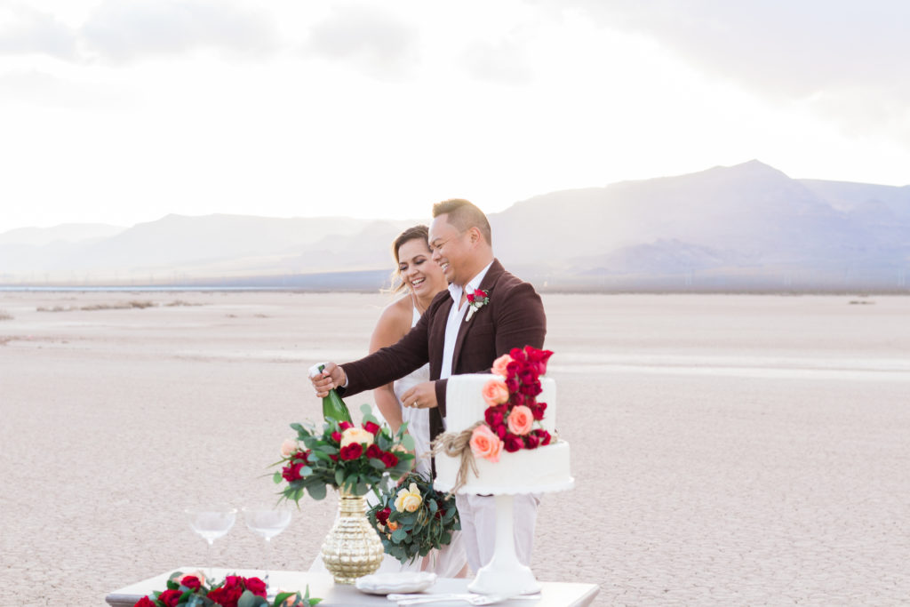 Bride and groom opening a bottle of champagne celebrating their elopement in Las Vegas at El Dorado Dry Lake Bed